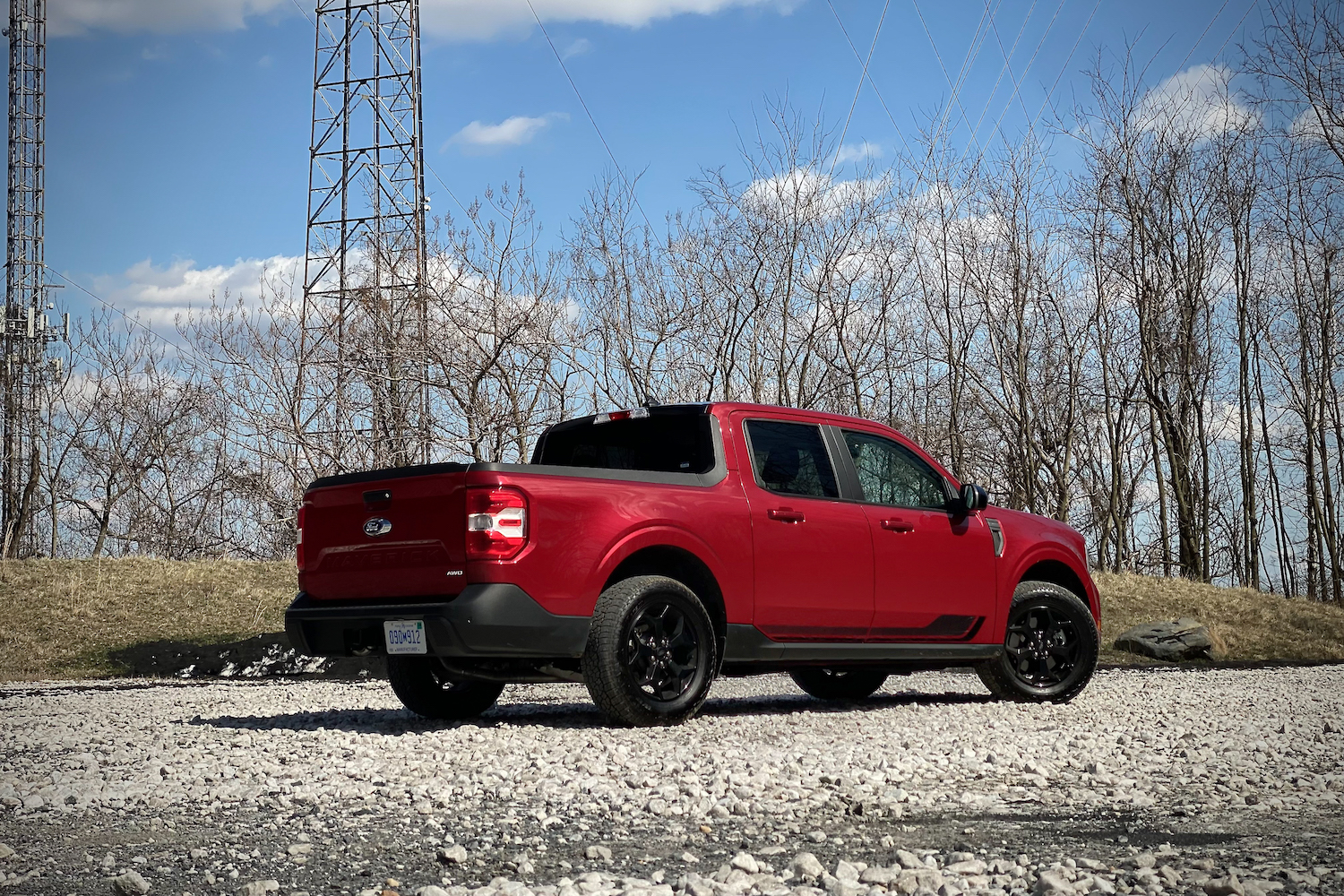 Rear end angle of 2022 Ford Maverick from passenger's side on a gravel parking lot with blue skies.