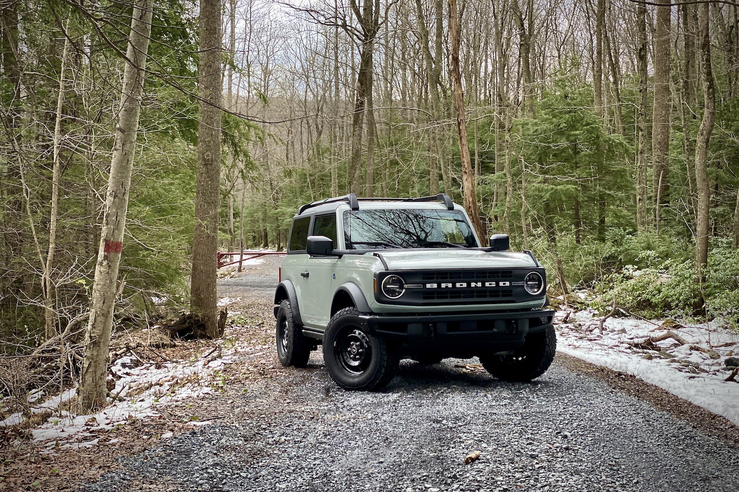 2021 Ford Bronco front end angle from passenger side on a gravel road in front of bare trees on a gravel trail.