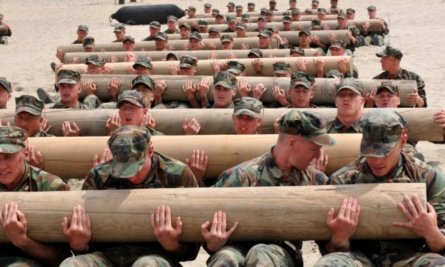 Soldiers group hold logs while performing sit-ups.