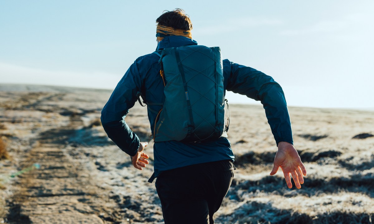 A close-up shot of a man running away from the camera. He is wearing blue jacket and carrying a blue backpack
