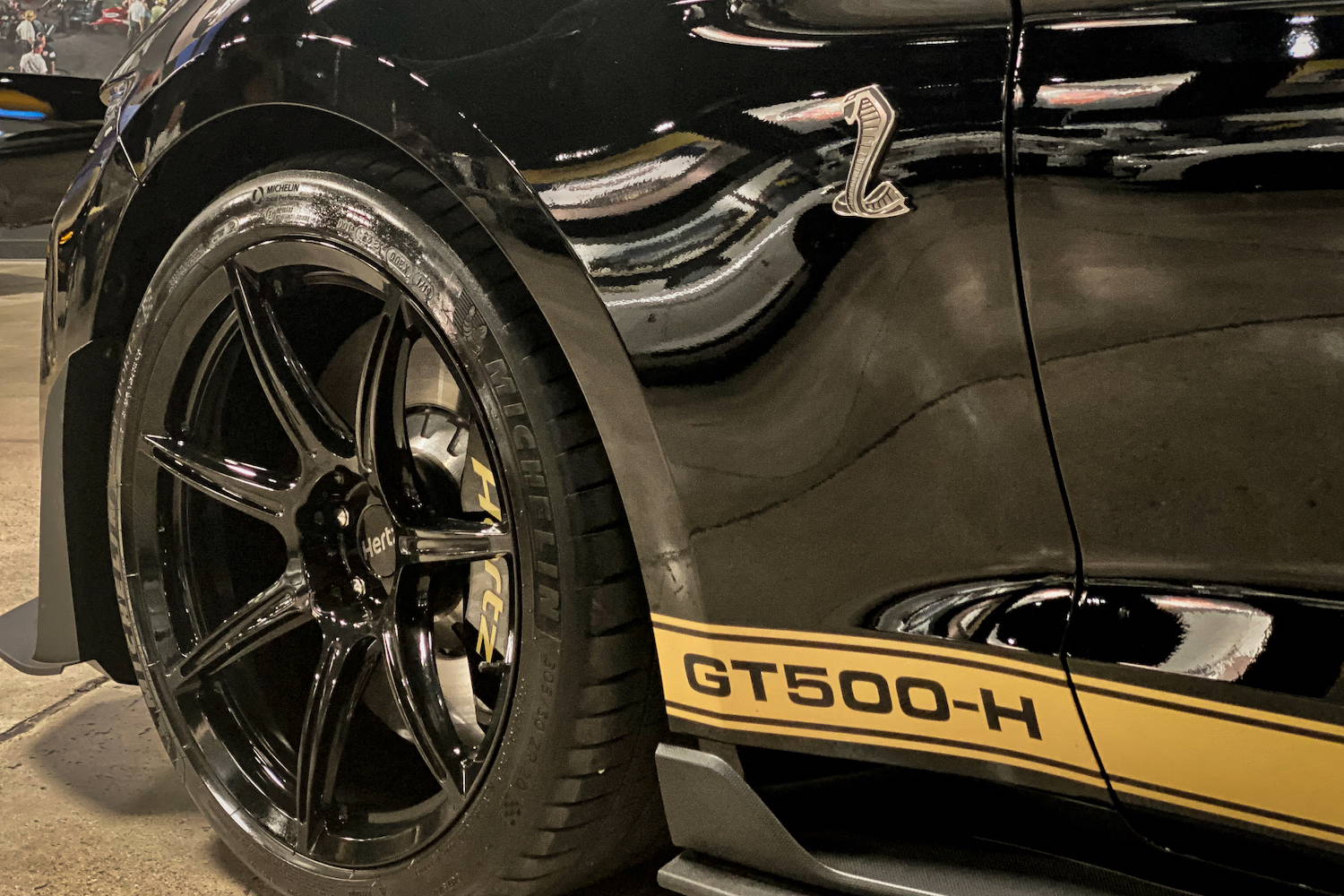 Close up of 2022 Shelby GT500-H badge and front left wheel in a garage.