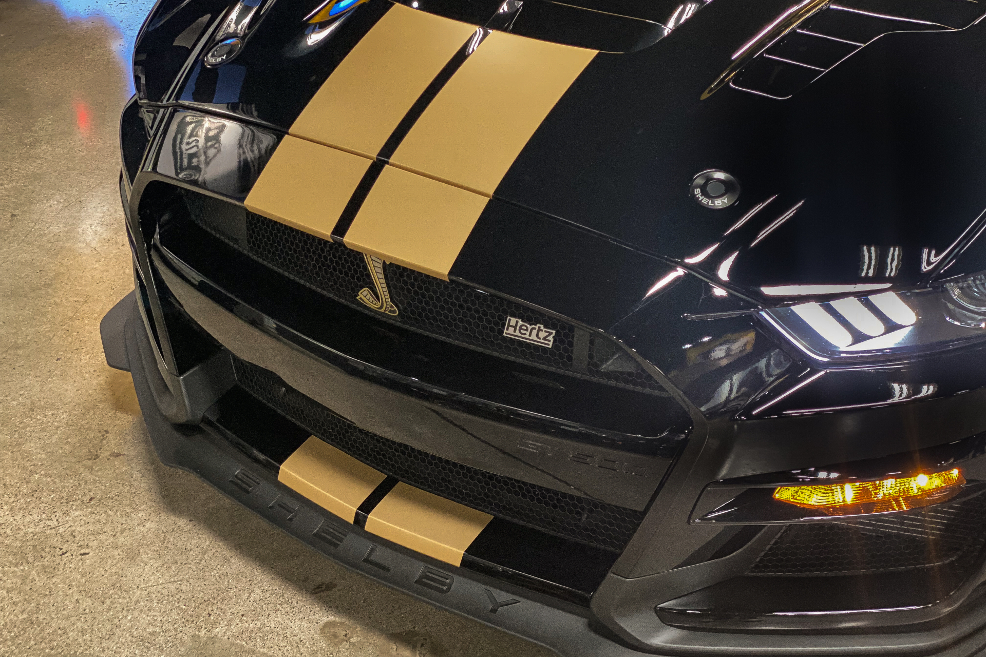 Close up of 2022 Shelby GT500-H front end from top view with gold stripes, grille, and headlights in a garage.