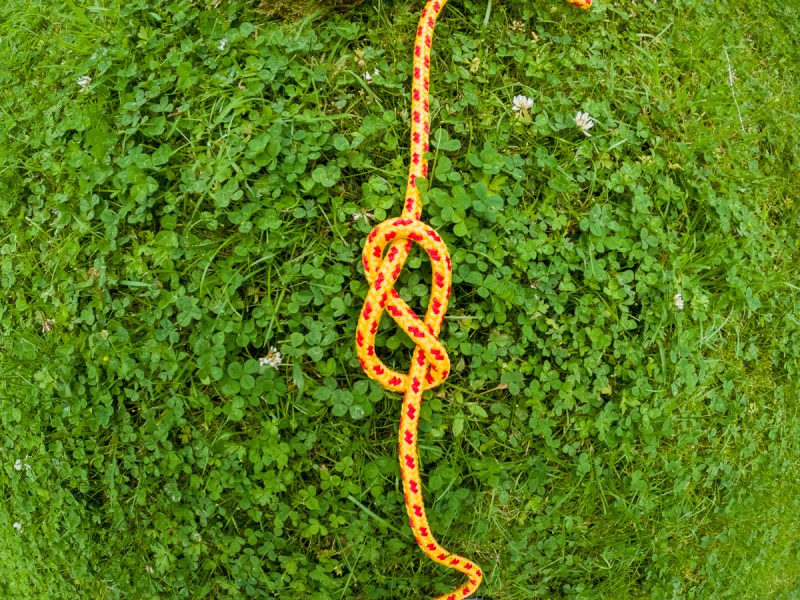 A single figure eight tied in yellow and red rope laid on the grass