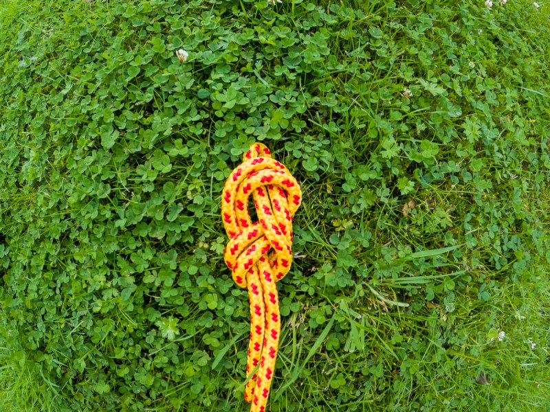 A fully tied double figure eight knot in yellow and red rope on the grass.