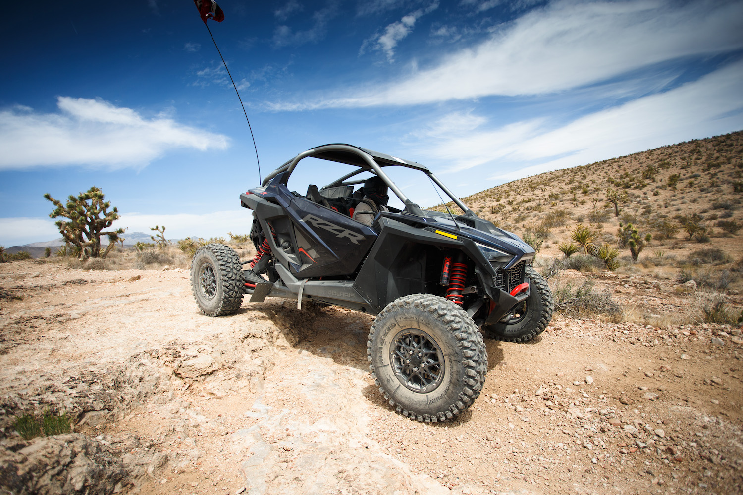 Close up of front left end of Polaris RZR Pro R driving down a rocky hill through the Mojave desert.