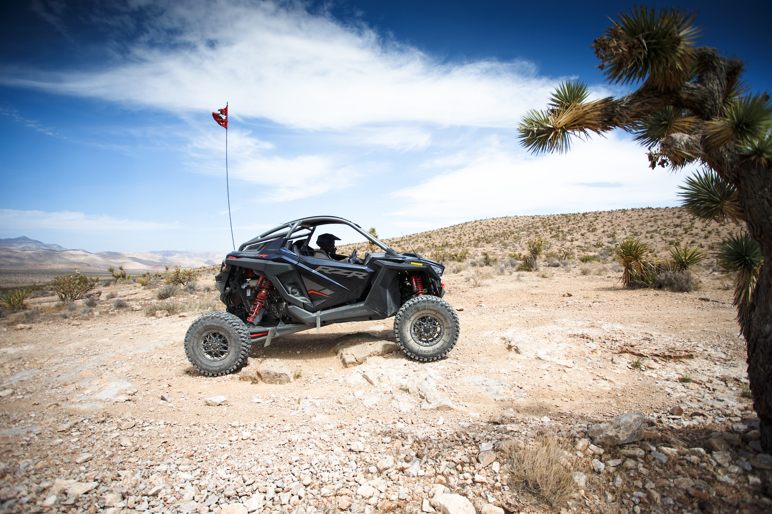 Side angle of Polaris RZR Pro R on a dirt path in the desert driving up a dirt path.