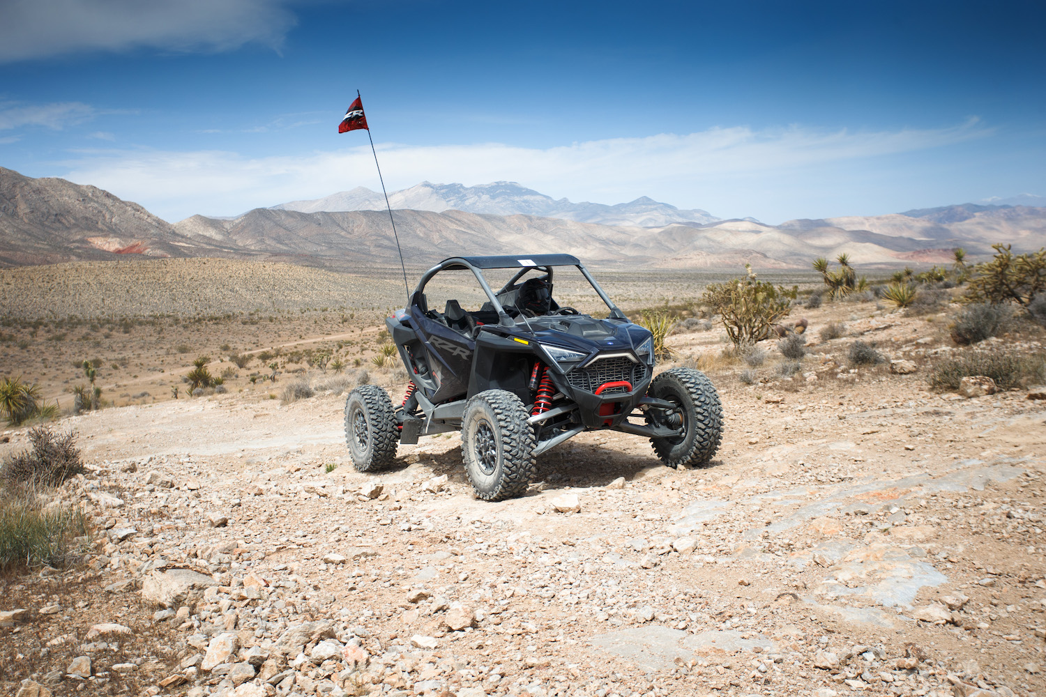 Close up of side angle of Polaris RZR Pro R driving on a rocky dirt trail with a mountain in the background.