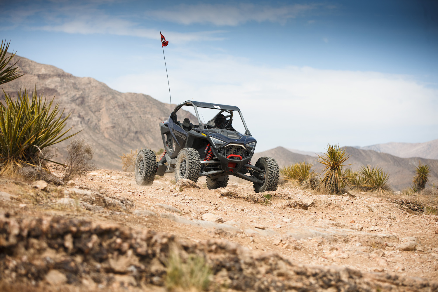 Front end angle of Polaris RZR Pro R in the desert going down a dirt hill with a mountain in the background.