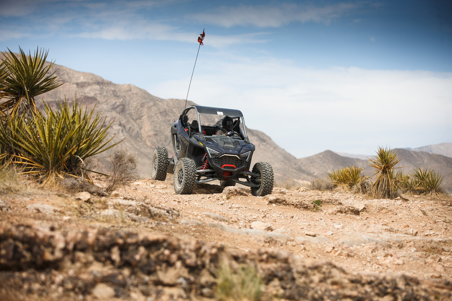 Polaris RZR Pro R going down in a hill on a dirt path in the desert with a mountain in the background.
