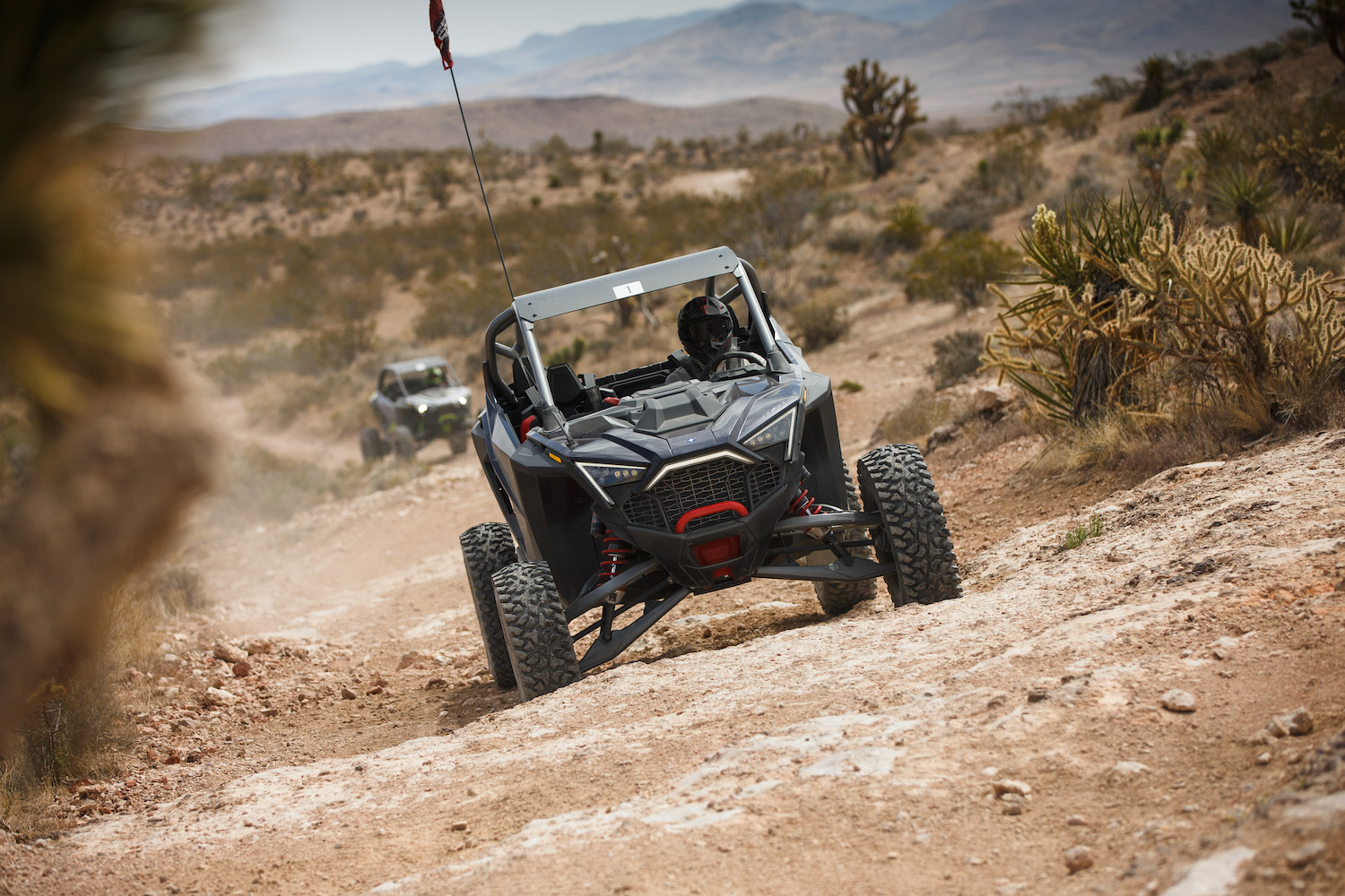 Close up of front end of Polaris RZR Pro R going up a hill in a desert on a dirt trail.