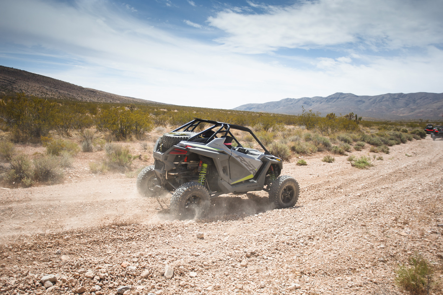 Rear end angle of Polaris RZR Turbo R on a dirt trail in the desert with mountains in the background.