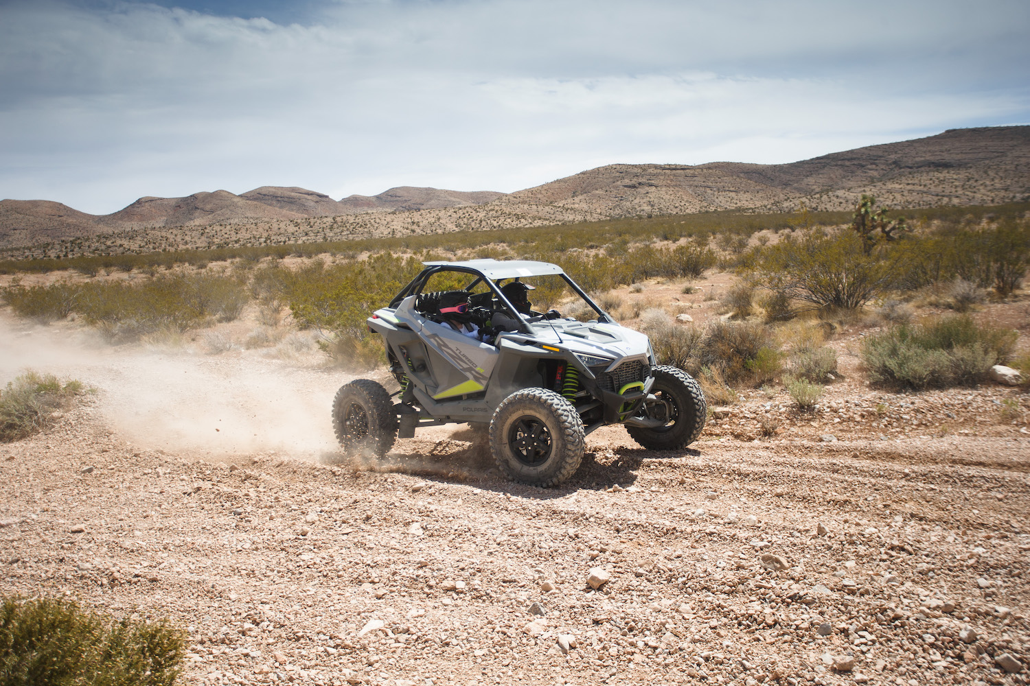 Close up of front end angle of Polaris RZR Turbo R throwing up dirt on a dirt trail in the desert.