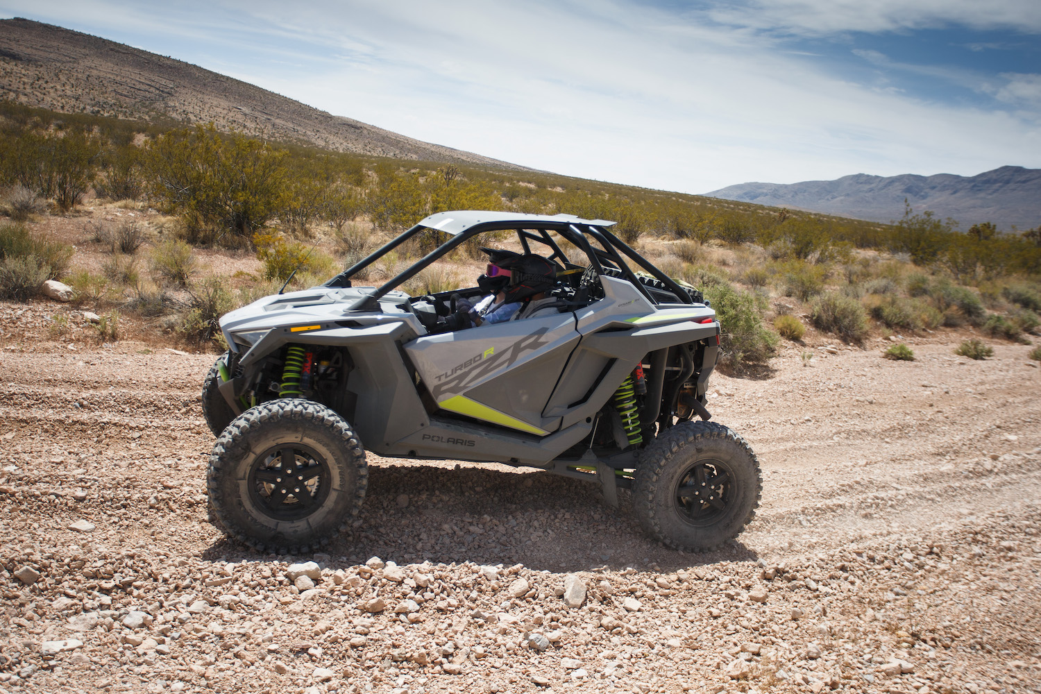 Polaris RZR Turbo R from the side on a dirt trail in the desert with bushes in the background.