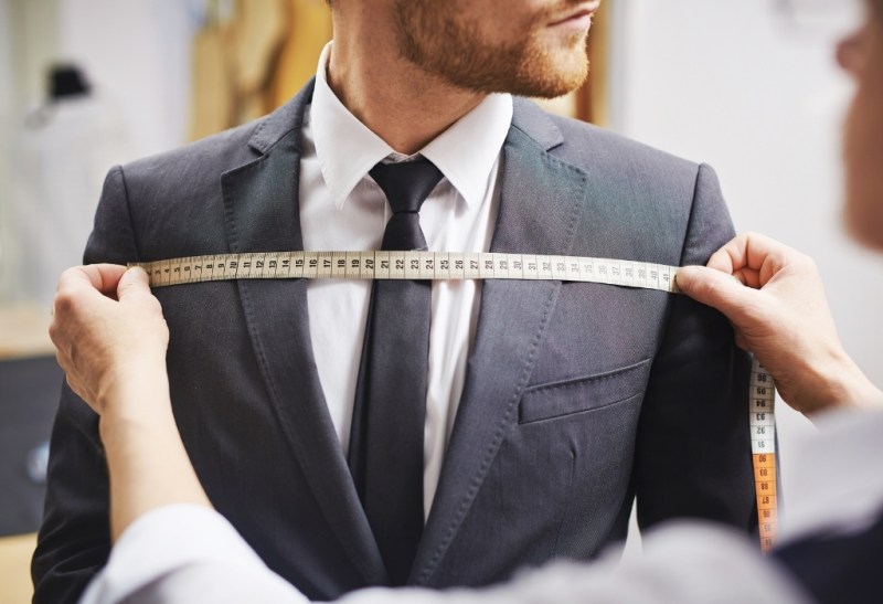 Tailor stretching measuring tape across suited chest