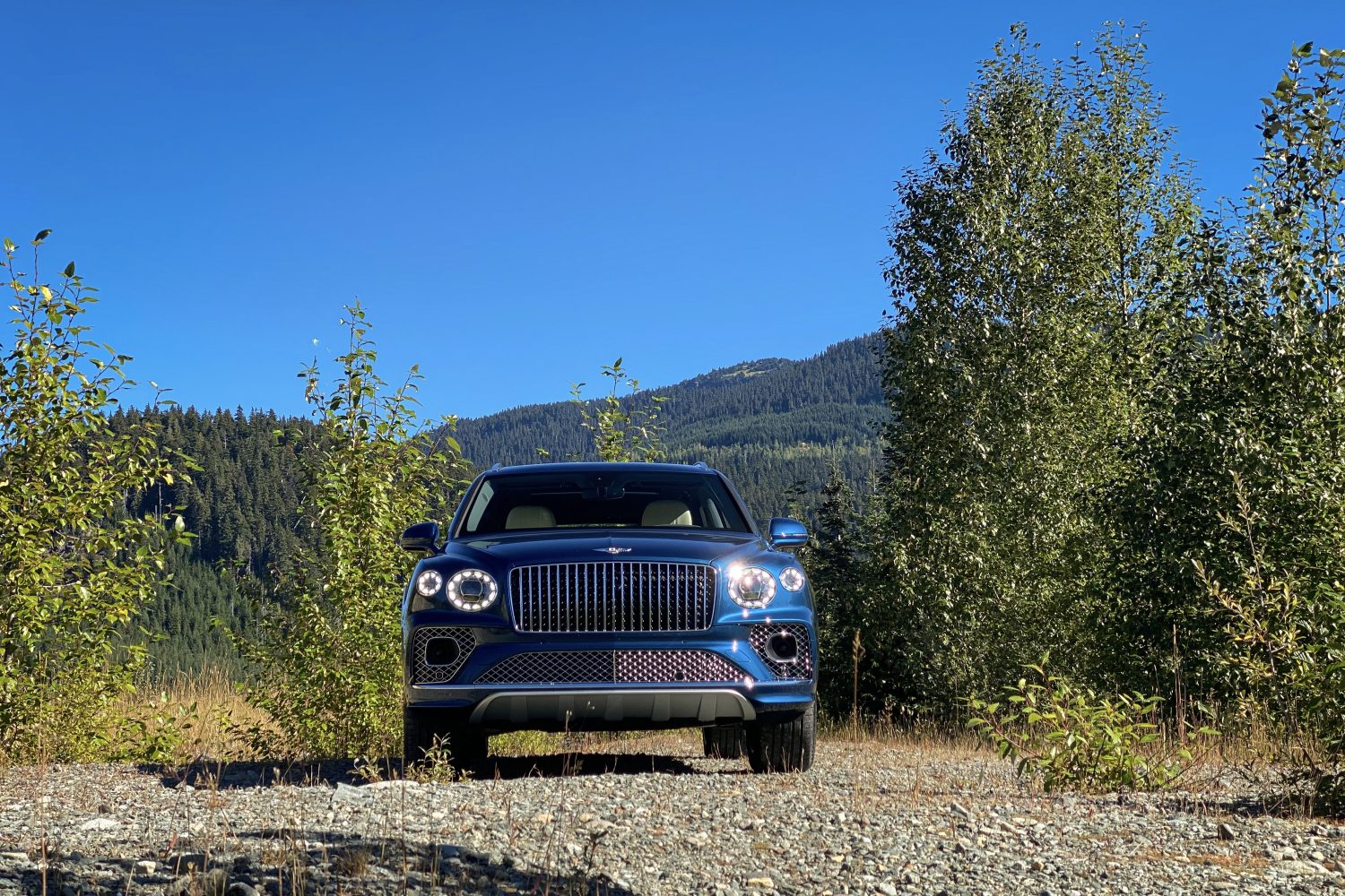 Close up of front end of 2023 Bentley Bentayga EWB from straight ahead with mountains and blue skies in the back.