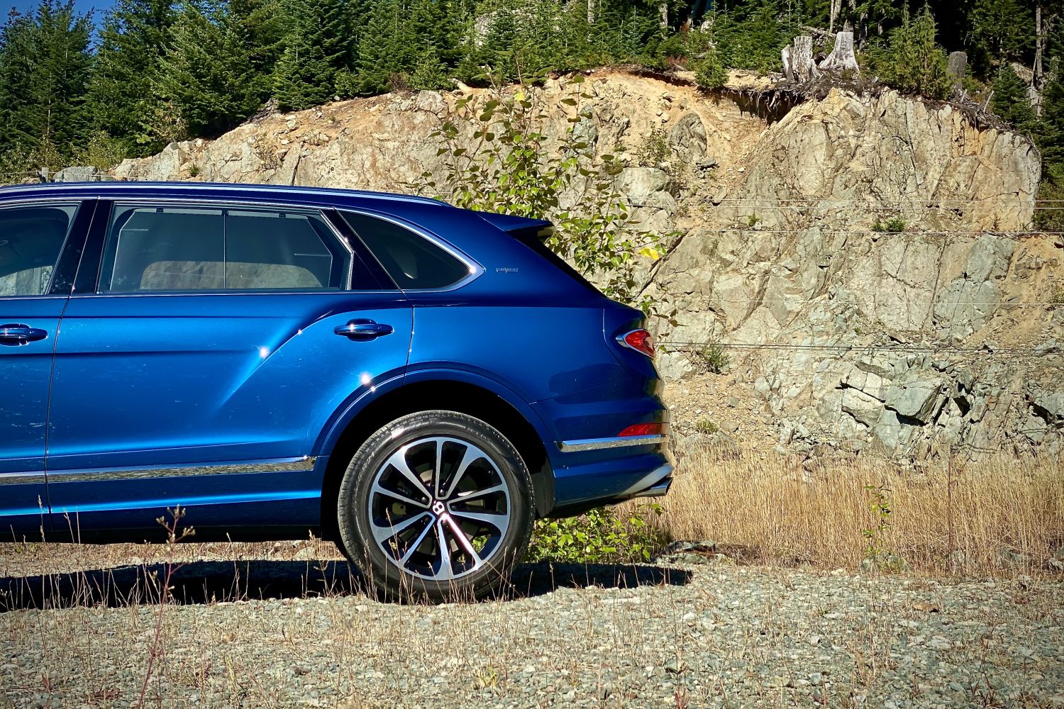 Back half of 2023 Bentley Bentayga EWB on a gravel path with a mountain in the back.