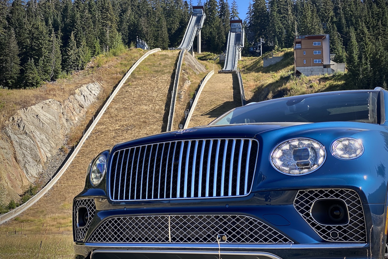 Close up of 2023 Bentley Bentayga EWB headlights and grille in front of ski jumps at Whistler Olympic Park.