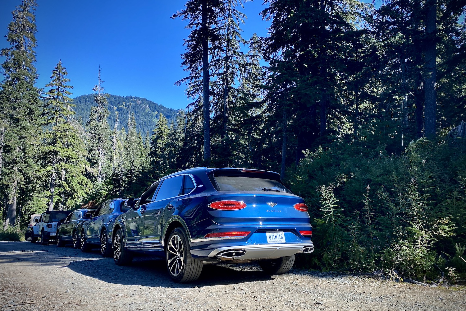 Rear end of 2023 Bentley Bentayga EWB in the middle of the woods in Whistler Olympic Park with trees in the back and on a gravel