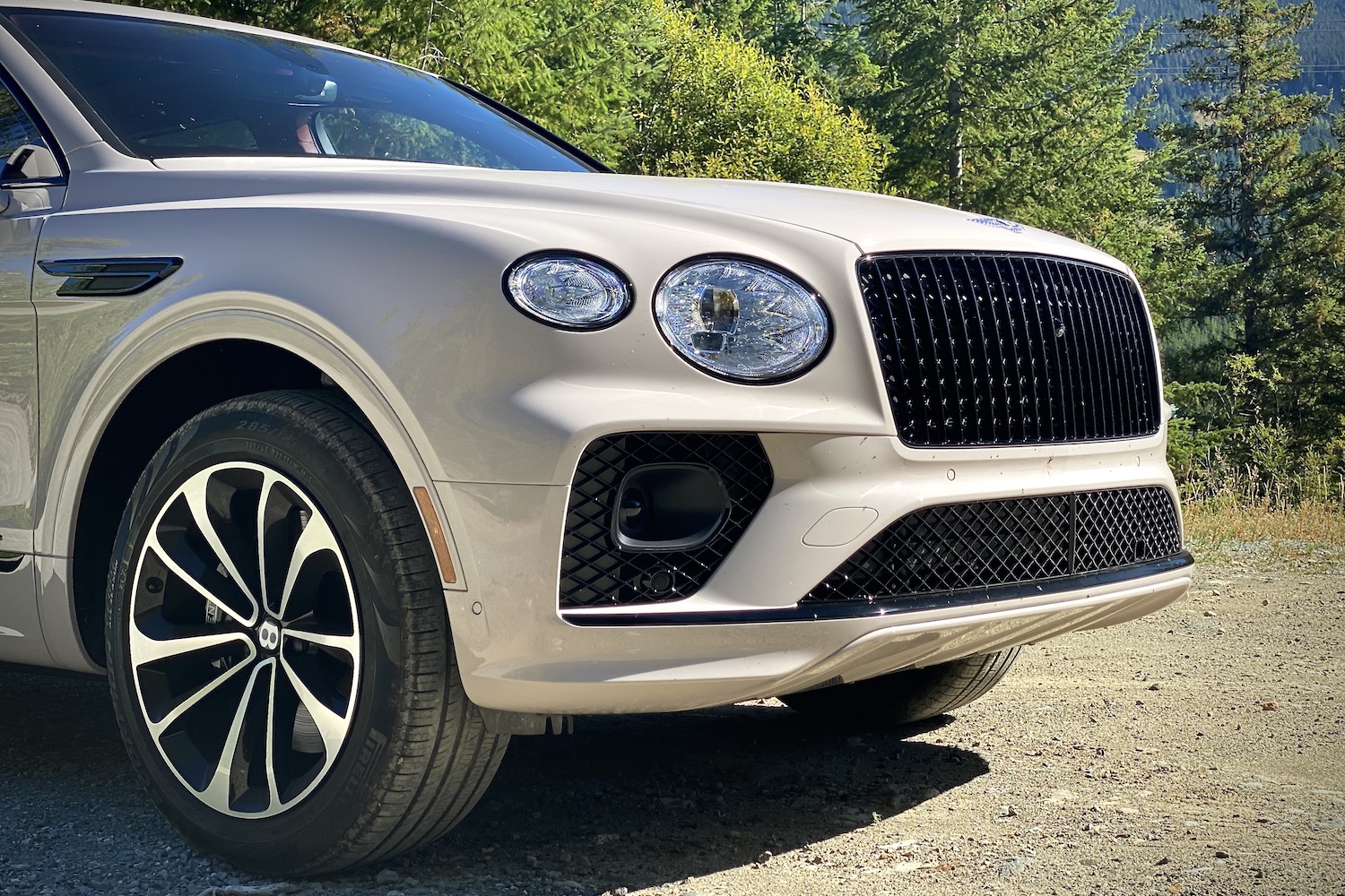 Close up front end angle of 2023 Bentley Bentayga EWB headlights and grille with trees in the back.