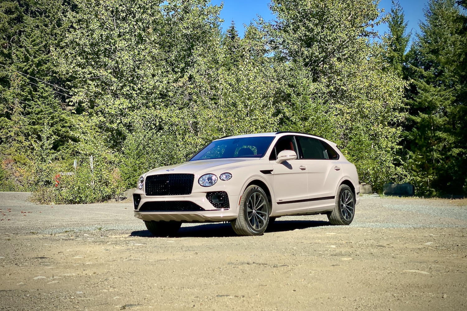 Front end of 2023 Bentley Bentayga EWB from driver's side angle on a dirt trail with trees in the back.