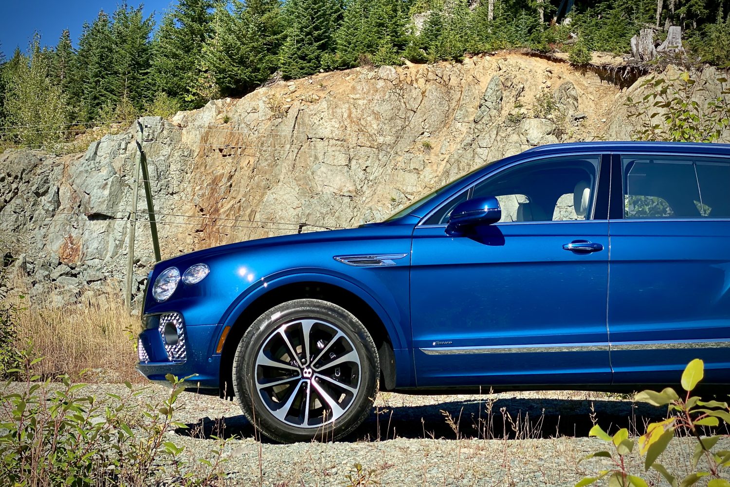 Front half of 2023 Bentley Bentayga EWB from driver's side with mountains in the back on a gravel road.
