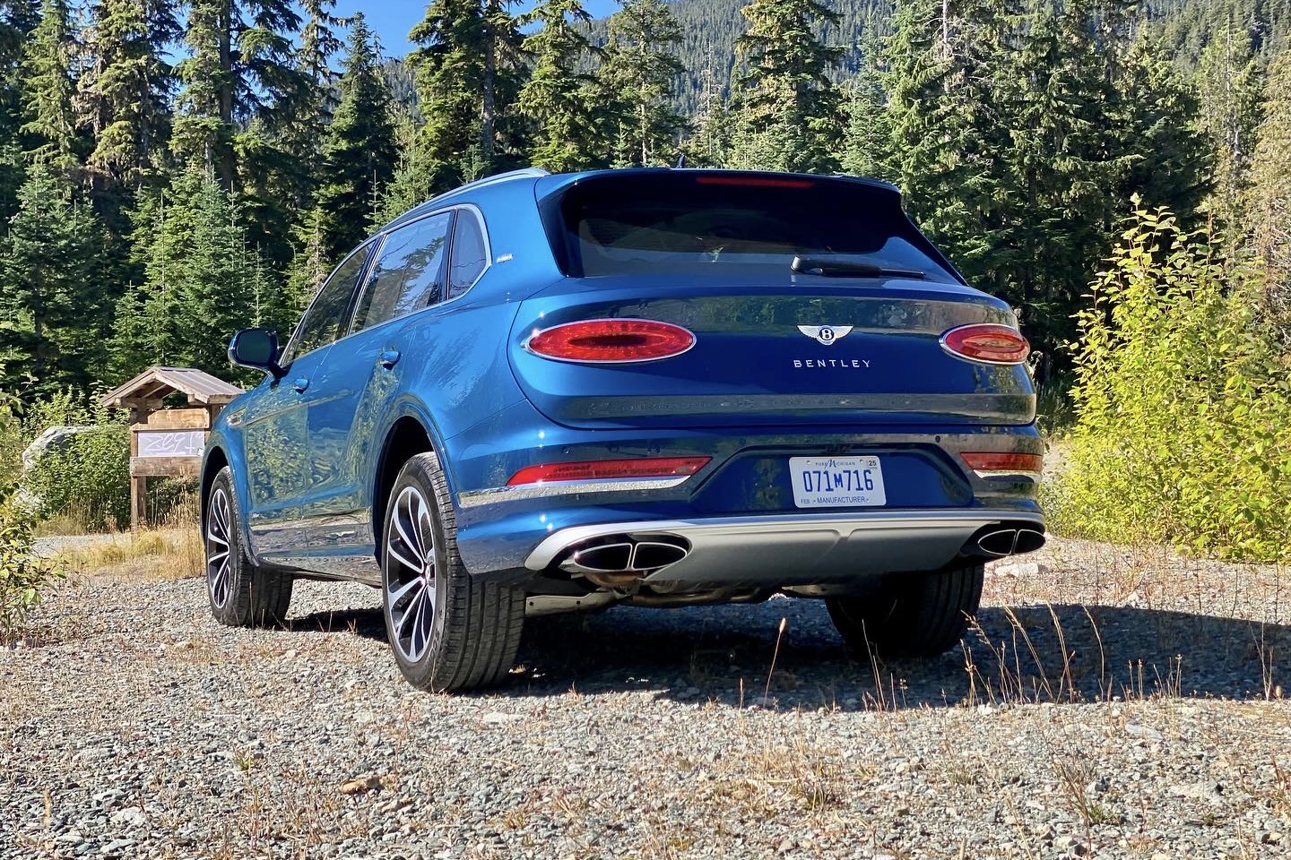 2023 Bentley Bentayga EWB rear end from driver's side on a gravel path with green trees in the back.