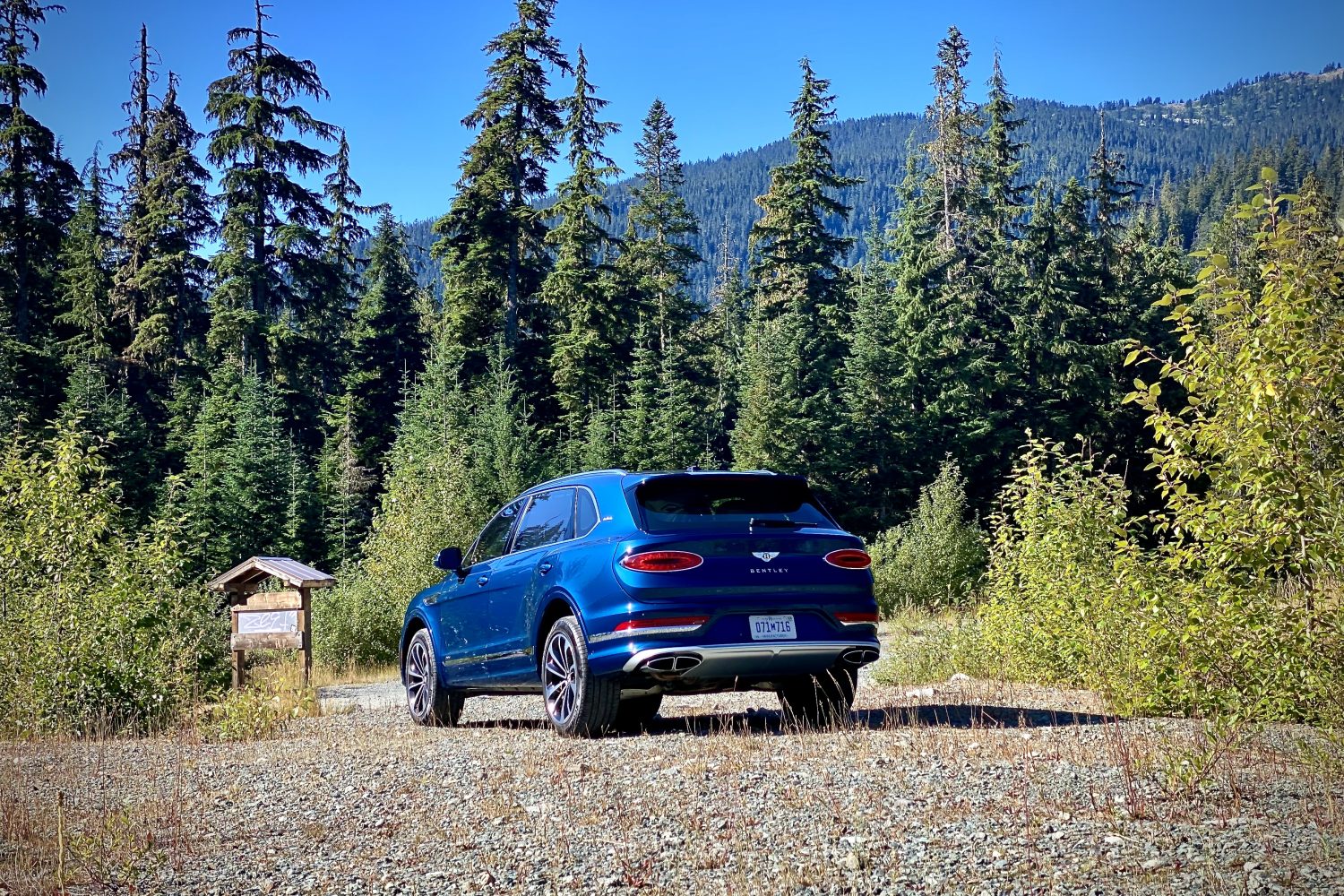 Rear end angle of 2023 Bentley Bentayga EWB from driver's side with green trees and a mountain in the back.