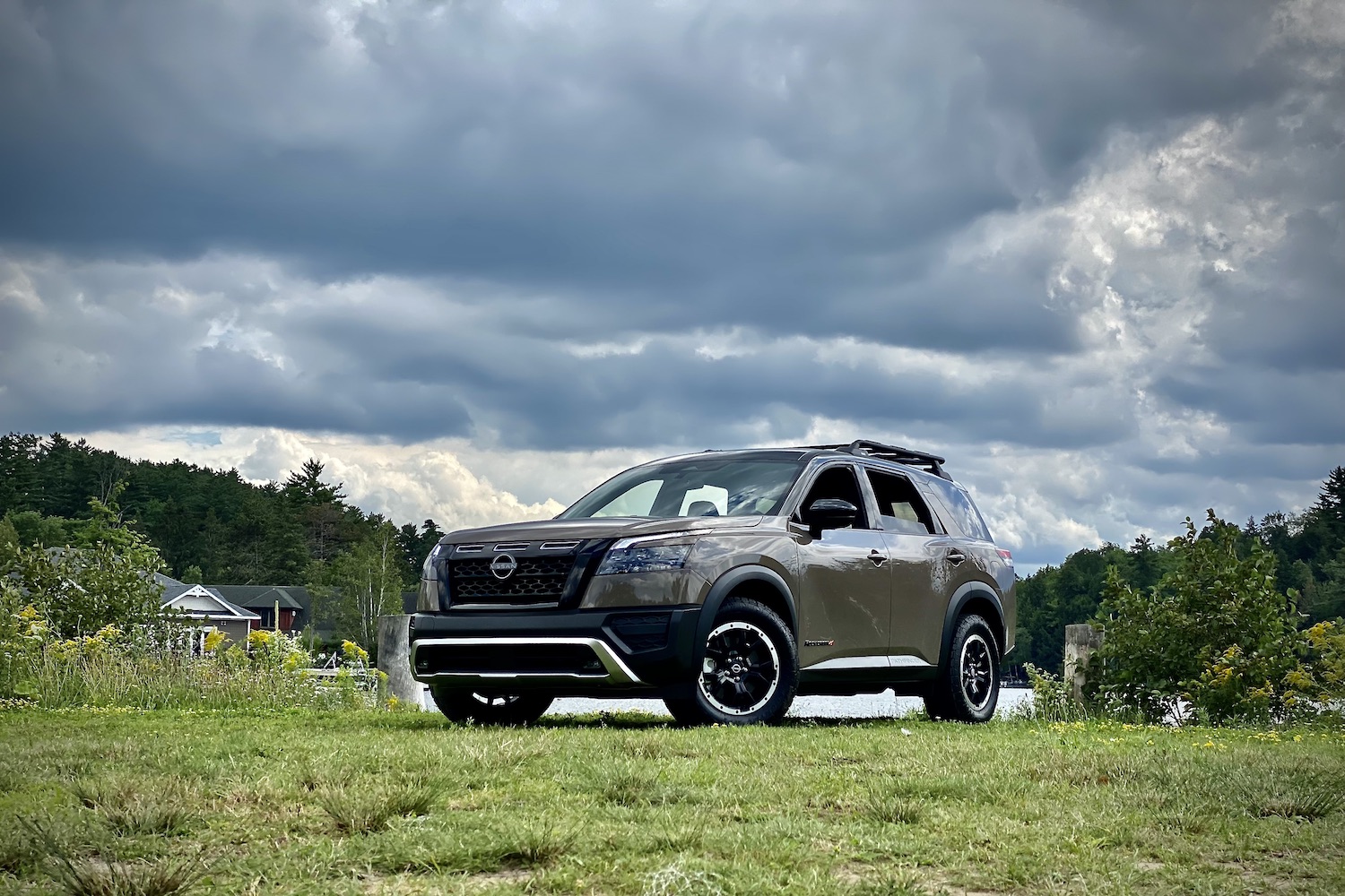 Front end angle of 2023 Nissan Pathfinder Rock Creek from driver's side in front of a lake on a grassy field with dark skies.