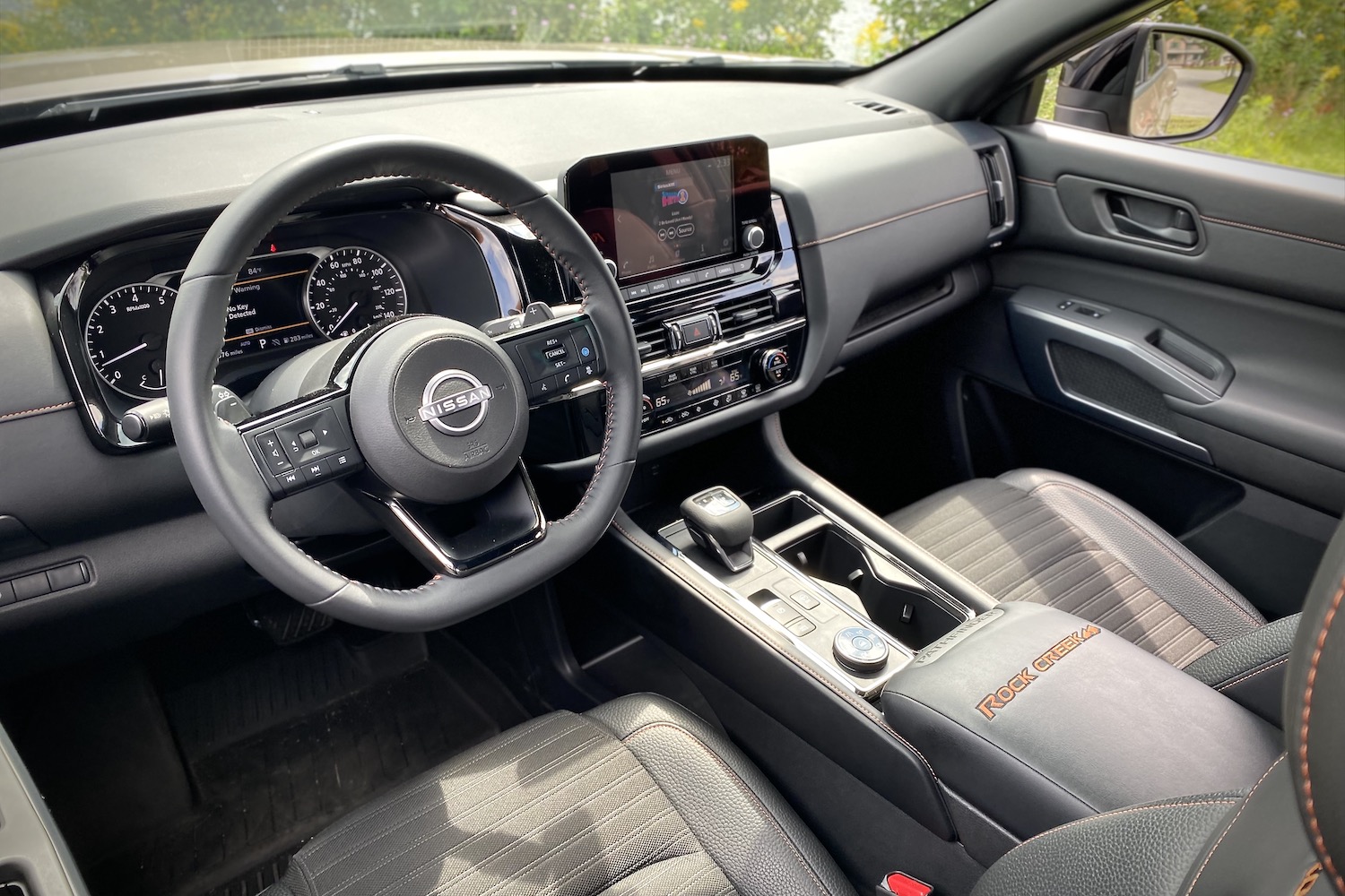 2023 Nissan Pathfinder Rock Creek dashboard and steering wheel in front of a grassy field.