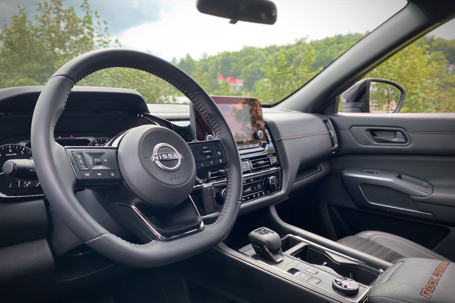 Close up of 2023 Nissan Pathfinder Rock Creek steering wheel with green bushes in the back.