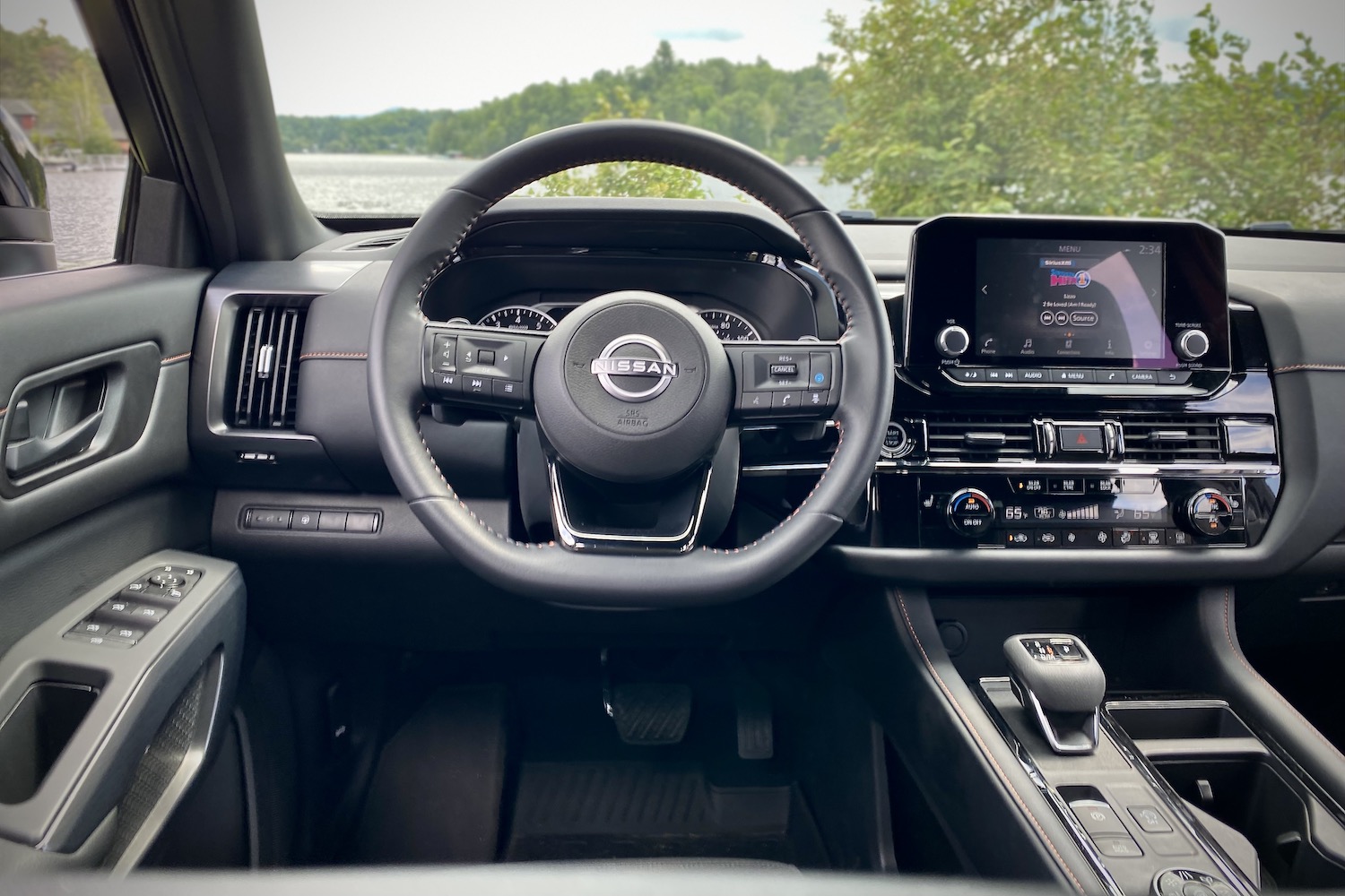 Close up of 2023 Nissan Pathfinder Rock Creek and center console from driver's seat with a lake and green trees.