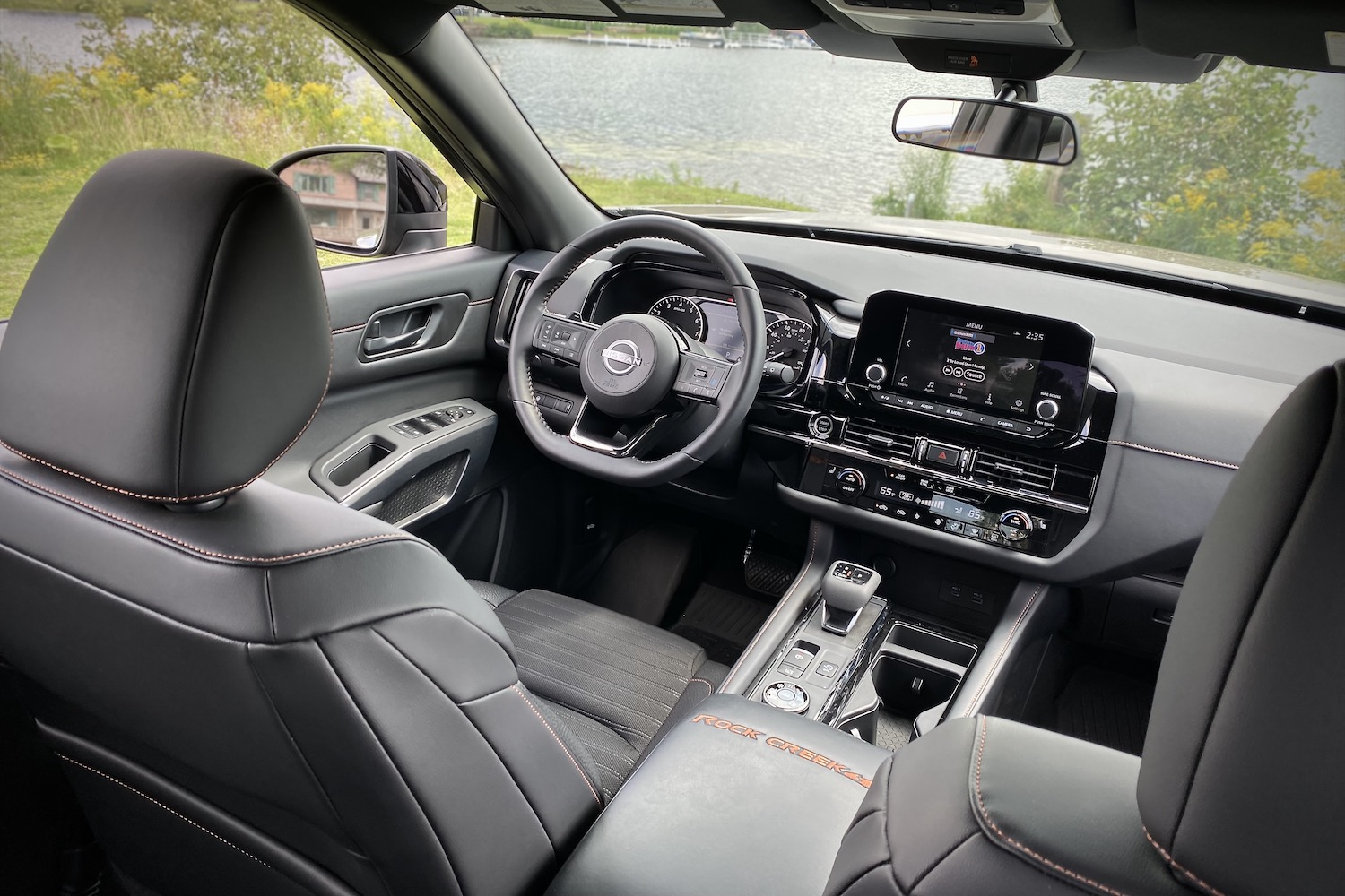 2023 Nissan Pathfinder Rock Creek dashboard and steering wheel from rear seats with a lake in the back.