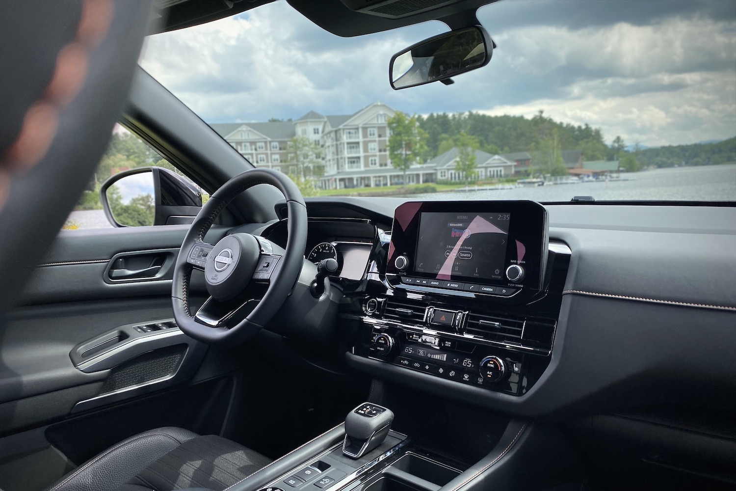 Center console and steering wheel in 2023 Nissan Pathfinder Rock Creek with hotel and lake in the back.