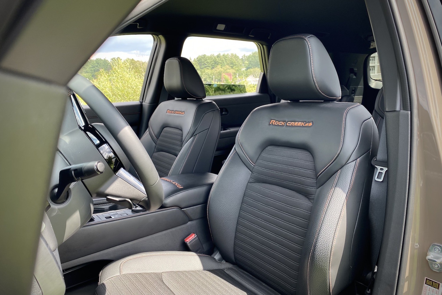 Front seats in the 2023 Nissan Pathfinder Rock Creek from outside with trees in the back.