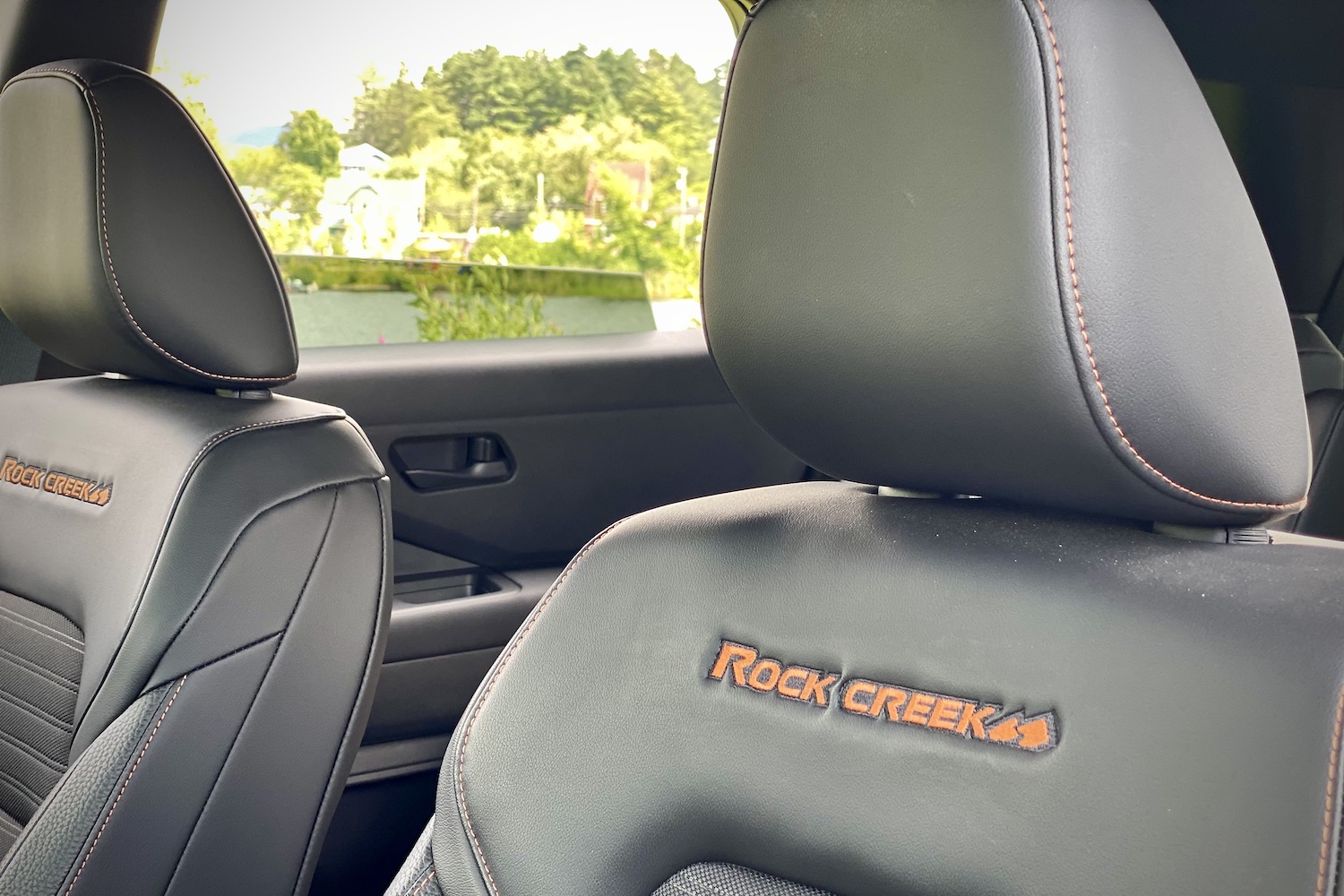 Close up of 2023 Nissan Pathfinder Rock Creek badges on front seats with trees in the back.