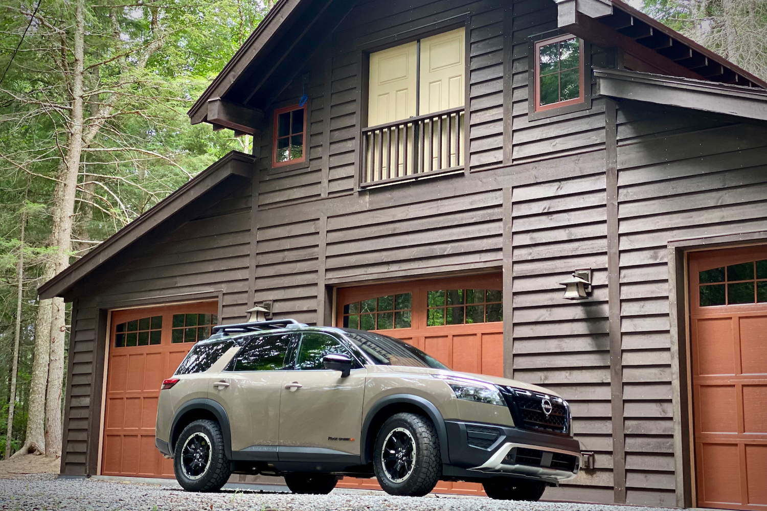 Front end angle of 2023 Nissan Pathfinder Rock Creek from driver's side in front of a lodge on a gravel road.