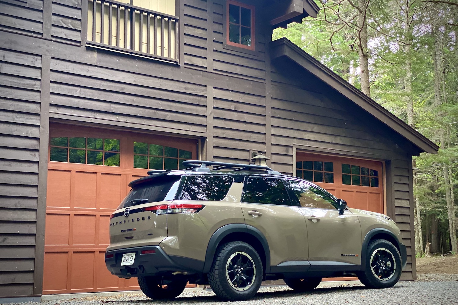 Rear end of 2023 Nissan Pathfinder Rock Creek from passenger's side on a gravel road in front of a lodge.