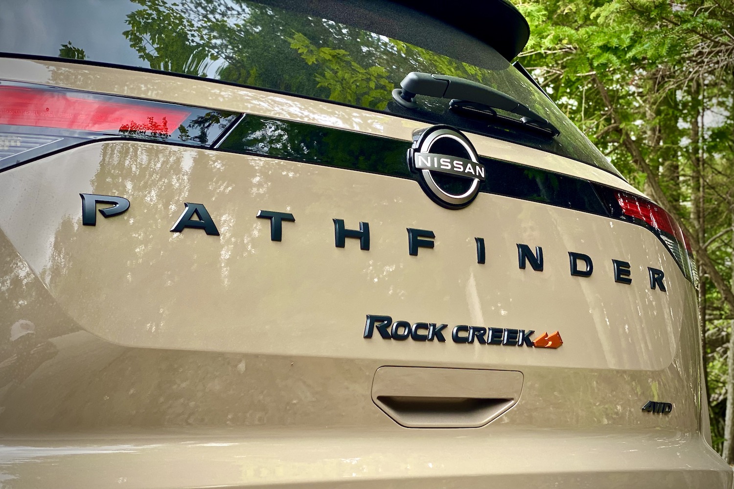 Close up of 2023 Nissan Pathfinder Rock Creek rear end badges in front of green trees.