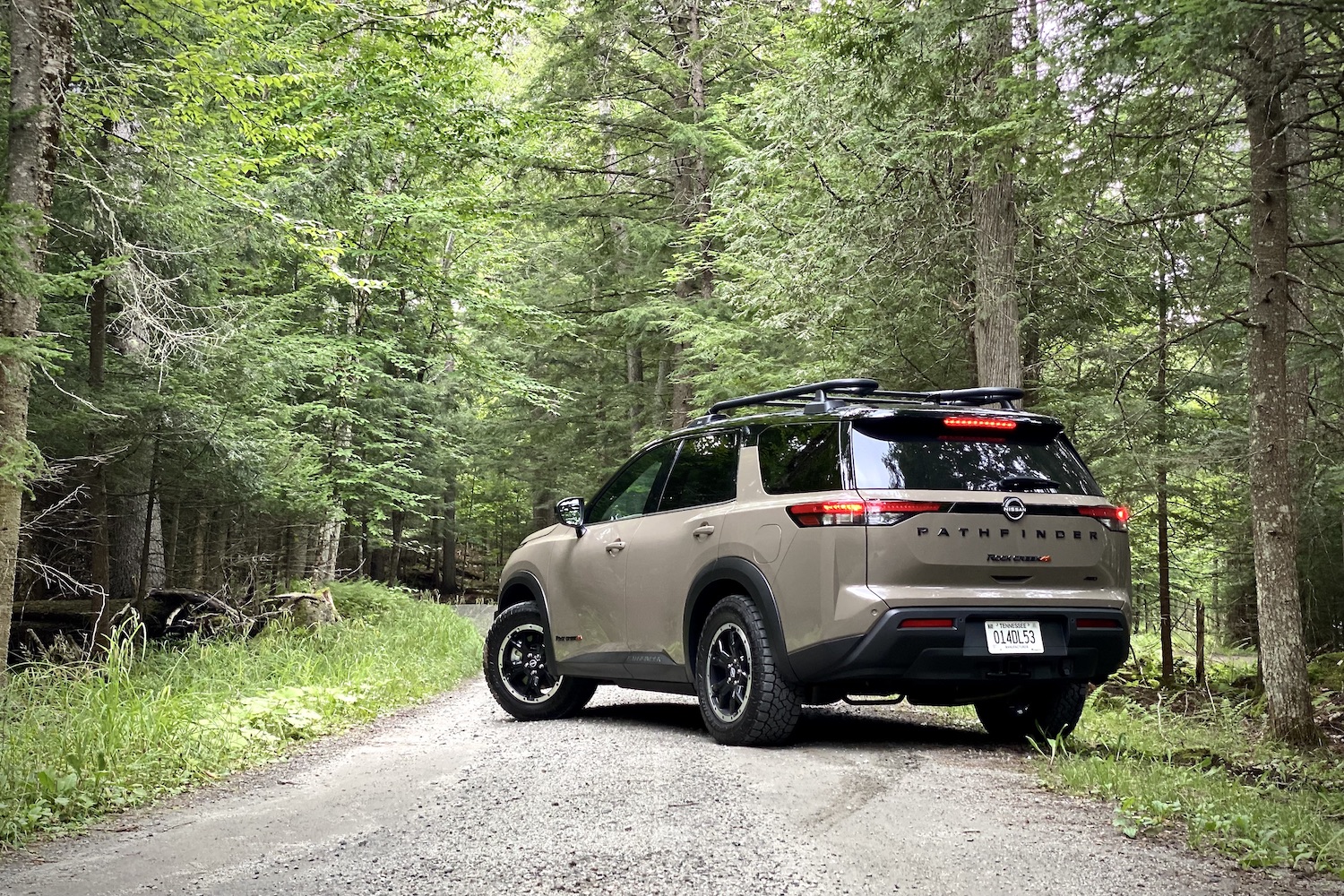 2023 Nissan Pathfinder Rock Creek on a dirt trail with trees on the side from the rear driver's side angle.