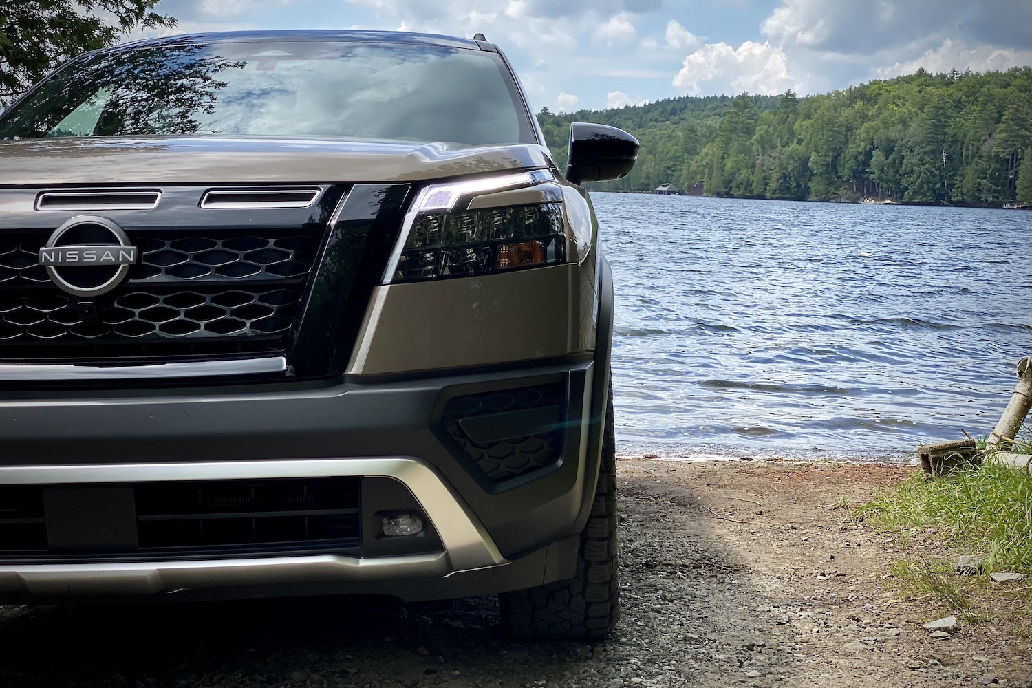 Close up of 2023 Nissan Pathfinder Rock Creek front end headlight and shield in front of a lake.