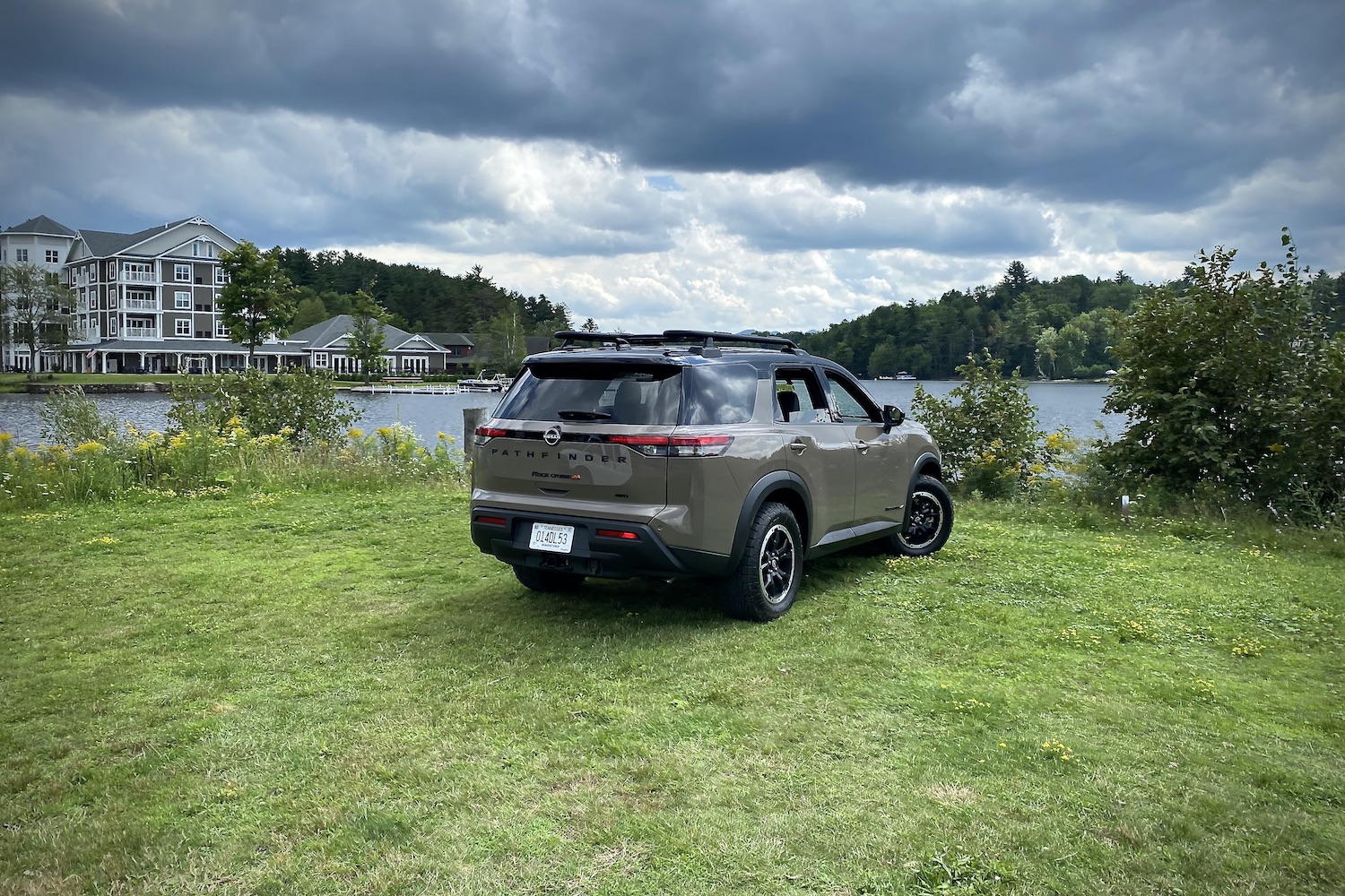 2023 Nissan Pathfinder Rock Creek rear end angle from passenger's side in front of a lake with dark clouds in the sky.