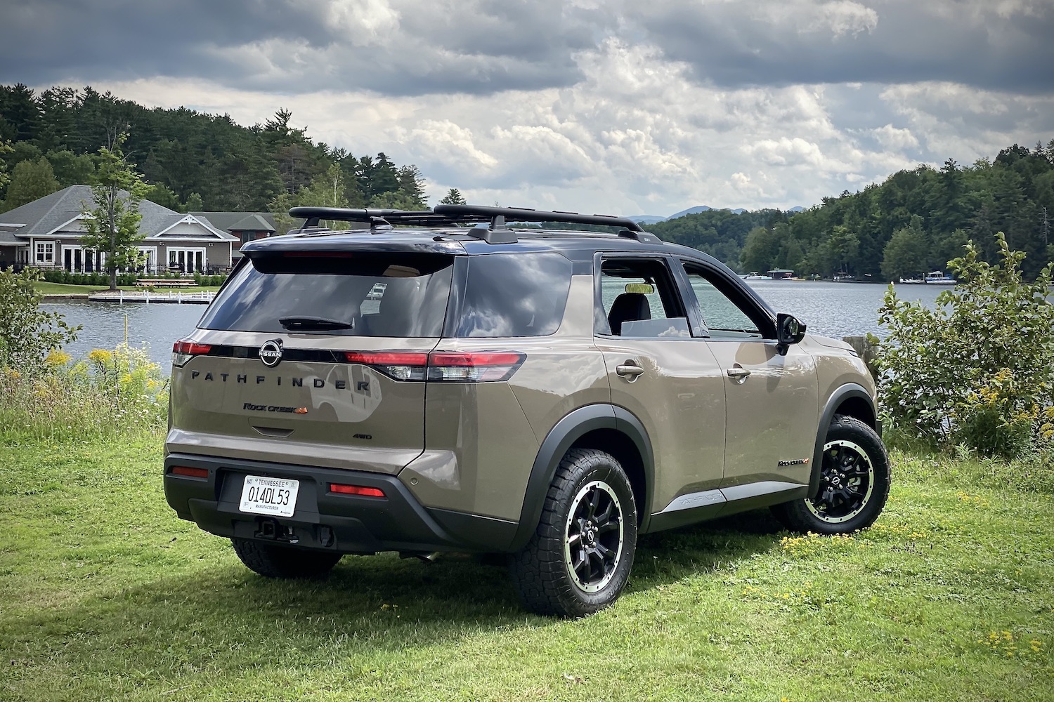 Rear end angle of 2023 Nissan Pathfinder Rock Creek from passenger's side with dark clouds in the back and a lake.