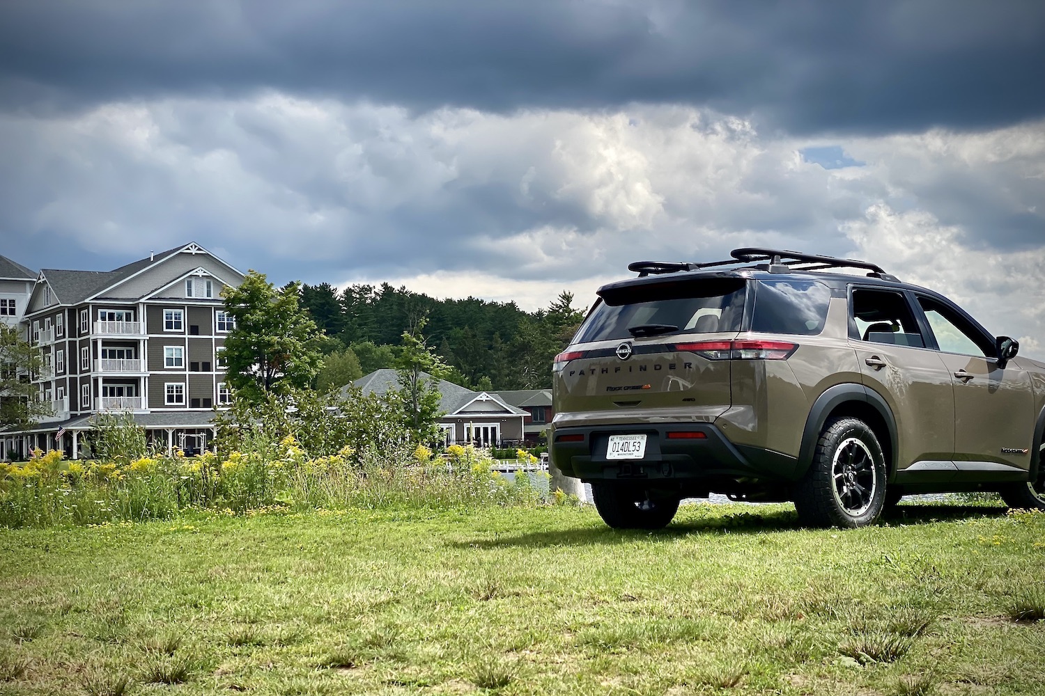 Close up of rear end of 2023 Nissan Pathfinder Rock Creek from rear passenger side angle with a hotel on a lake in the back.