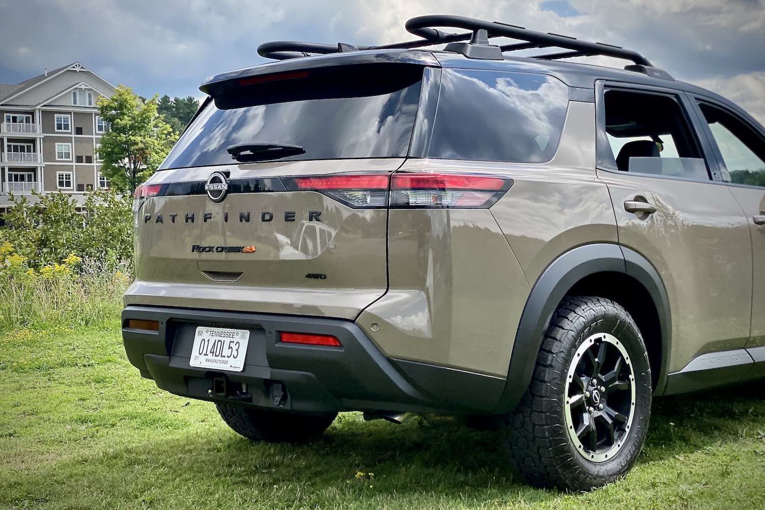 Close up of rear end of 2023 Nissan Pathfinder Rock Creek from passenger's side angle with a lake and hotel in the back on a gra