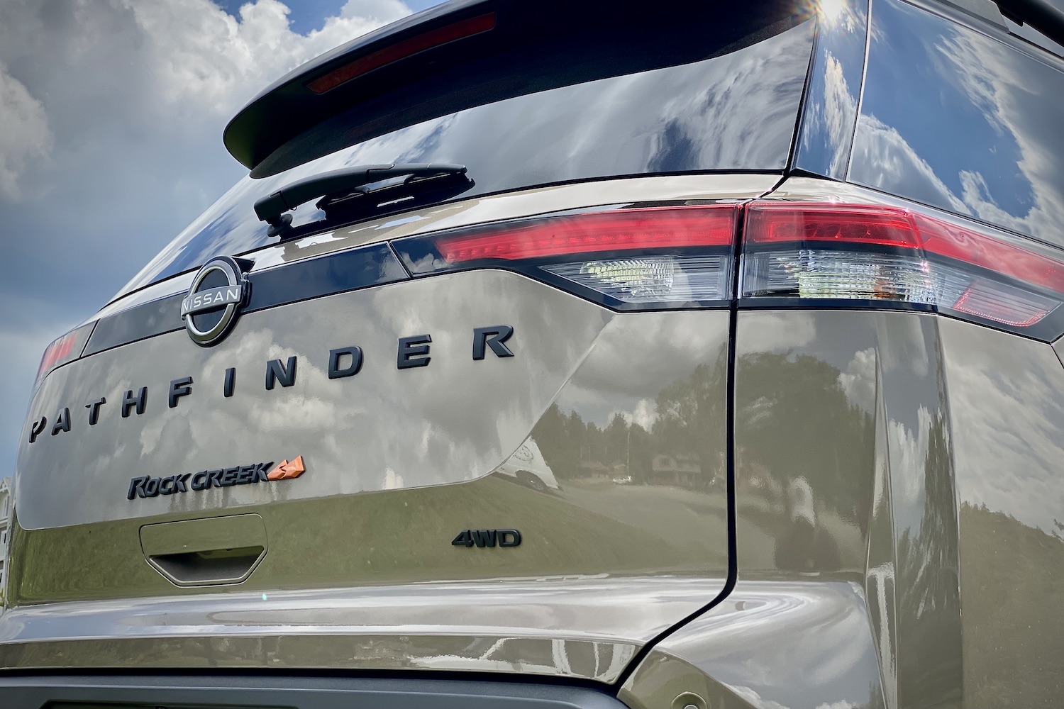 Close up of rear 2023 Nissan Pathfinder Rock Creek badges and taillights on a grassy field with dark skies.