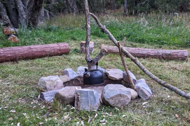 A campfire pot hanger holds a kettle over a stone circle