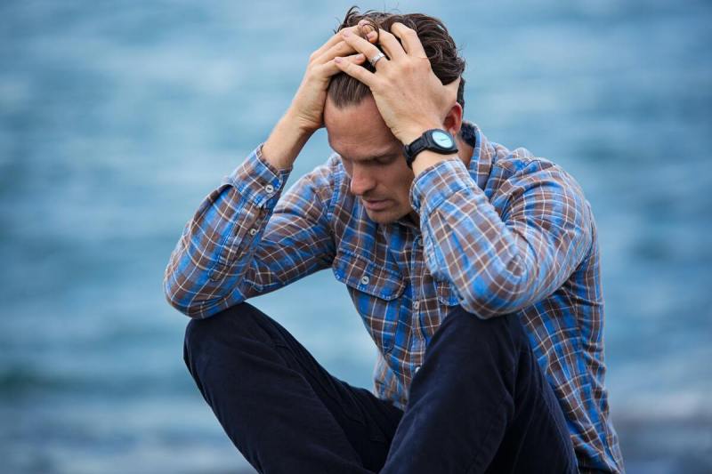 Depressed man near water sitting down.