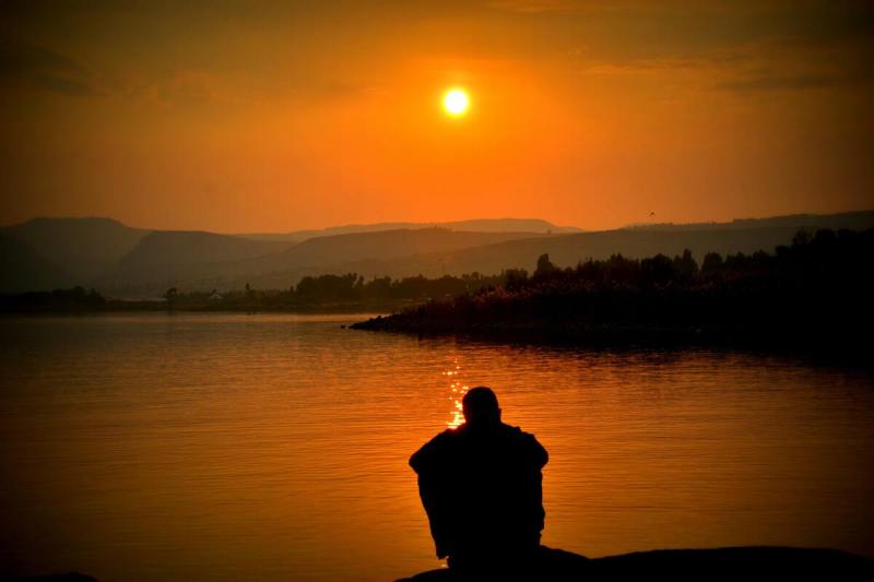 Man sitting on edge of lake.