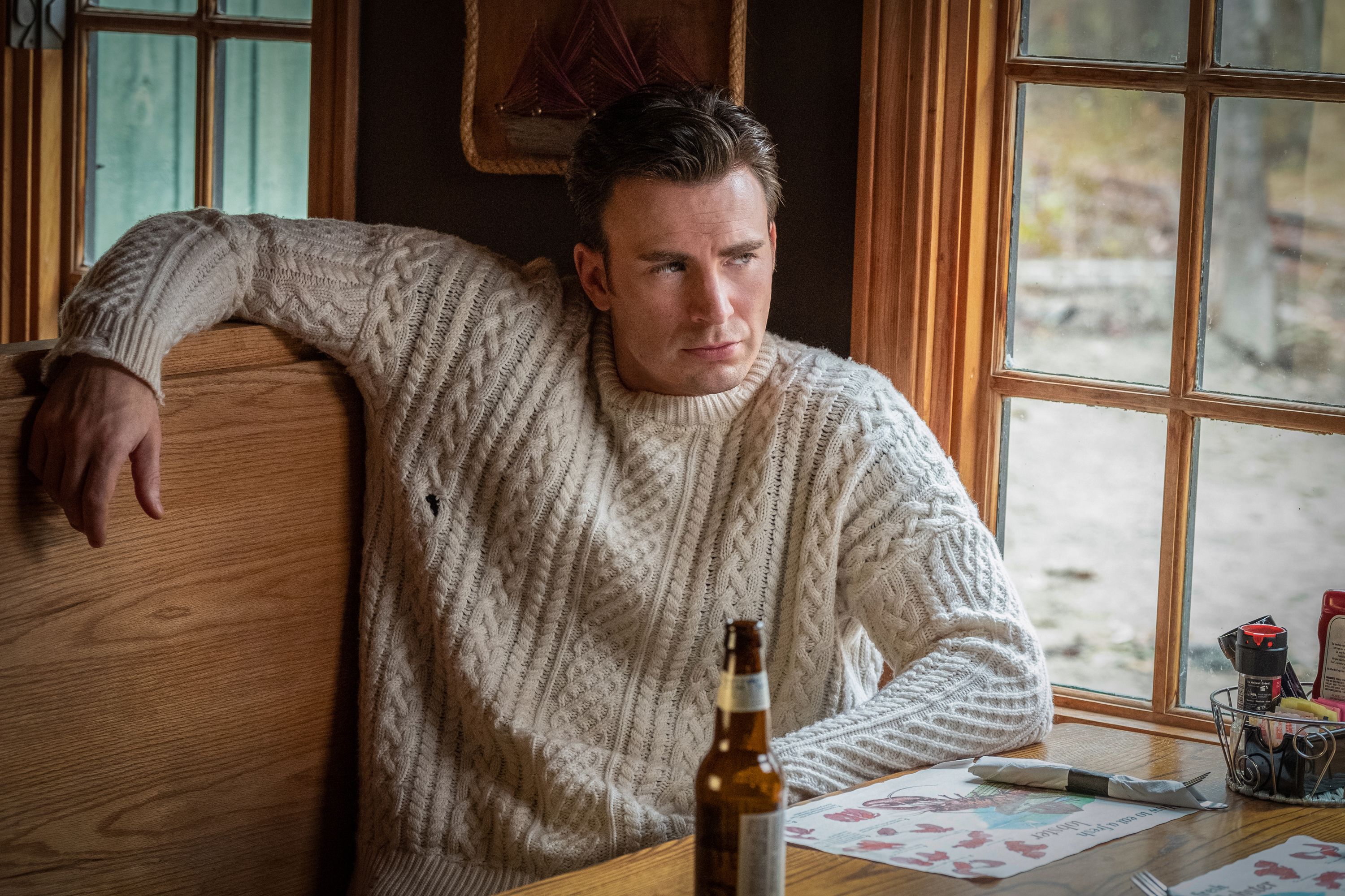 Chris Evans sitting at a table in a chunky knit sweater
