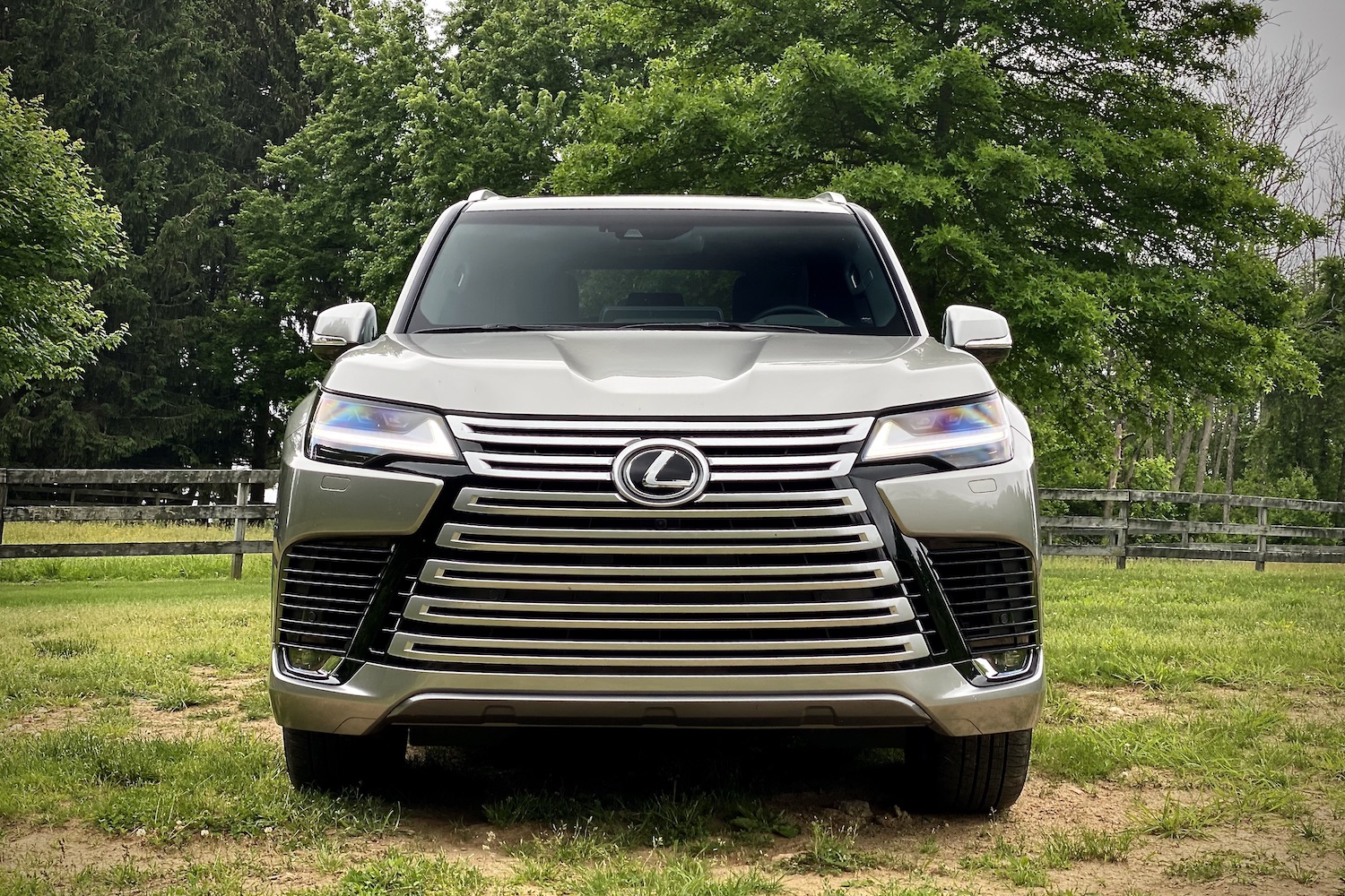 Close up of 2022 Lexus LX 600 front end on a patchy field of grass with trees in the back.